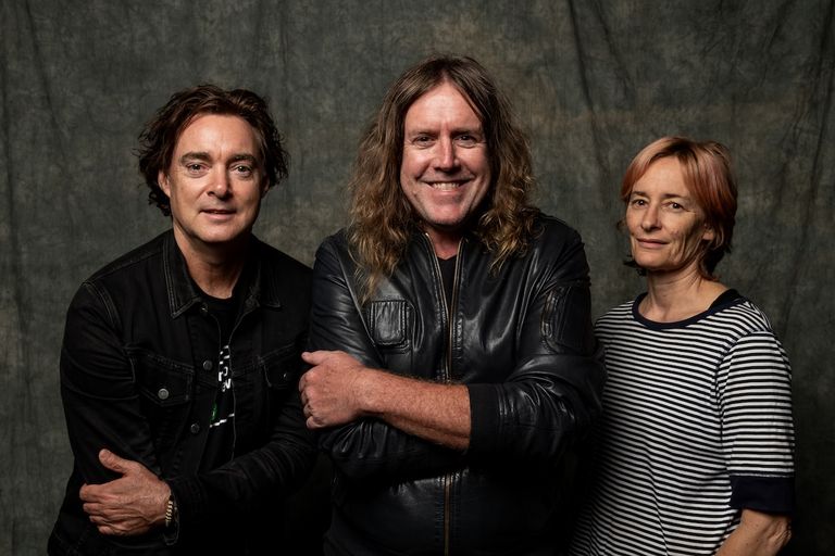 Australian rock band Spiderbait members Whitt, Kram, and Janet English posing together against a textured grey background.